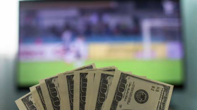 Men's hands keep money dollars against the background of a TV set on which football is playing, close-ups, gain